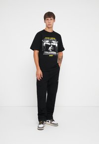 Sort bomulds T-shirt med grafisk print, parret med sorte cargo bukser med flere lommer, og hvide sneakers med grå detaljer.