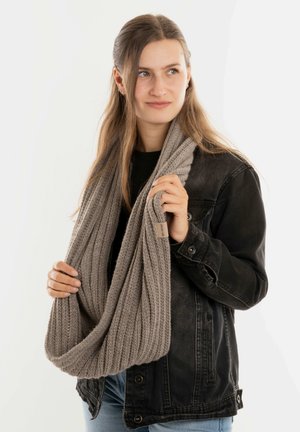 Lichtgrijze gebreide infinity-sjaal vastgehouden door een persoon, met een geribde textuur, zacht materiaal en een klein label aan één kant.