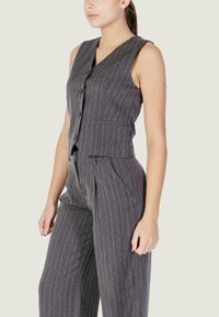 Gilet grigio a righe sottili con scollo a V, chiusura con bottoni e tasche laterali, abbinato a pantaloni a gamba larga coordinati, realizzati in tessuto strutturato.