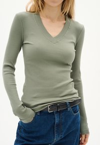 Olivgrön ribbad långärmad topp med V-ringning, kombinerad med högmidjade blå denimjeans och ett svart bälte.