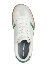 Zapatilla blanca con acentos verdes y detalles de ante. Presenta una superficie texturizada y cordones planos. Suela de goma con un logo visible en el interior.
