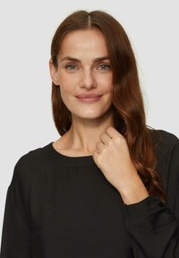 Czarna bluzka z szerokim dekoltem i długimi, lekko bufiastymi rękawami. Gładka faktura z luźnym krojem, z delikatnym połyskiem.