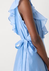 Light blue dress featuring ruffled sleeves, a smooth texture, and a tie at the waist. The fabric has a soft sheen and flowing design.
