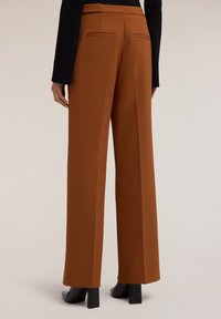 Bruine wijde broek met een gladde textuur, voorzien van achterzakken en een gestructureerde tailleband, gecombineerd met zwarte hoge hakken.