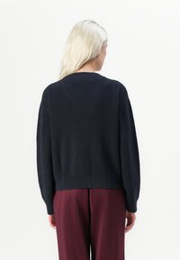 Dark navy knitted sweater with a ribbed texture, featuring a round neckline and dropped shoulders, paired with burgundy trousers.