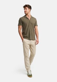 Olijfgroene shirt met korte mouwen van textuurstof, beige linnen broek en groene sneakers, met een ontspannen pasvorm en een dichtgeknoopte halslijn.