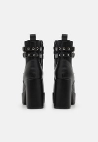 Botine negre cu toc au un finisaj din piele netedă, un design cu dublă curea dotat cu detalii din metal argintiu și un toc pătrat masiv.