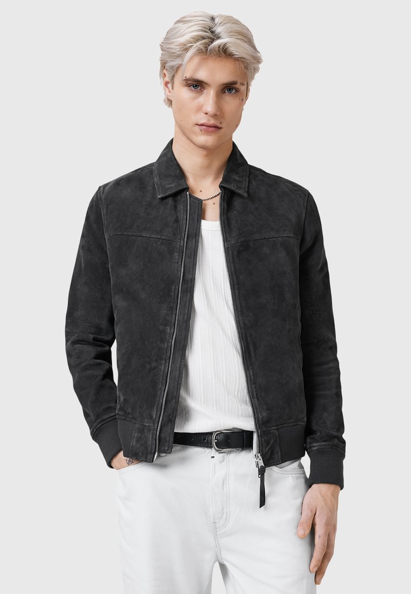 Schwarze Wildleder-Bomberjacke mit Reißverschluss, Kragen und gerippten Bündchen. Strukturiert Oberfläche mit schlanker Passform, getragen über einem weißen gerippten Shirt.