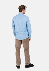 Helles blaues Baumwollhemd mit Knopfmanschetten und einem leicht abgerundeten Saum, kombiniert mit khakifarbenen Hosen und schwarzen Schuhen.