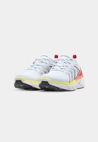 White athletic shoes with mesh upper, gray accents, colorful sole featuring yellow and red highlights, and a textured rubber outsole.