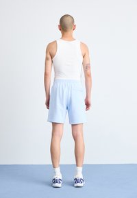 Lyseblå, bomuldsblandingsshorts med elastisk talje og baglomme, parret med en hvid tank top. Sneakers med lilla accenter.