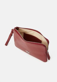 Červená kožená clutch taška so striebornými doplnkami, zipsovým uzáverom a vnútornou kapsou. Hladká textúra, malý zápästný popruh, obdĺžnikový tvar.