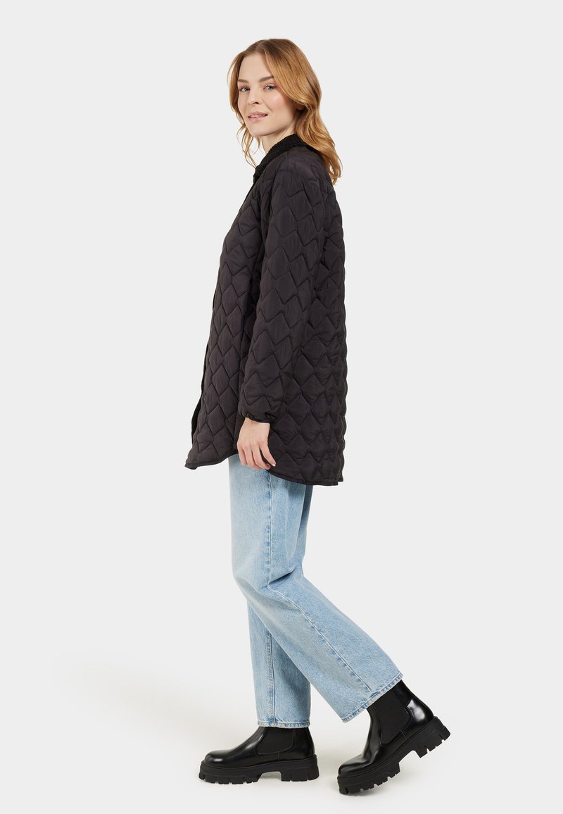 Schwarze gesteppte Pufferjacke mit rundem Kragen, langen Ärmeln und lockerer Passform. Kombiniert mit hellblauen geraden Jeans und schwarzen klobigen Stiefeln.