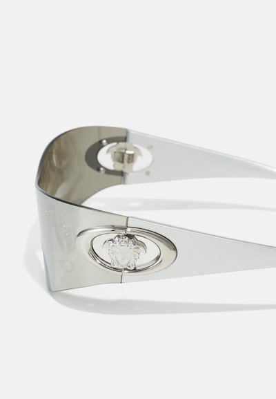 Silberne Sonnenbrille mit einzigartigem Wrap-around-Design, ausgestattet mit einem grauen Farbton und einem metallischen Medusa-Emblem-Detail am Rahmen.