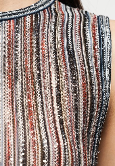 Αμάνικο τοπ με πολύχρωμες κάθετες ρίγες σε μεταλλική κλωστή, διακοσμημένο με παγιέτες, δημιουργώντας μια υφή και αντανακλαστική επιφάνεια.