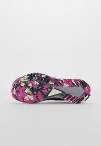 Semelle d'une chaussure de sport avec un motif camouflage noir, rose et beige et une bande de roulement rainurée pour l'adhérence sur fond blanc plat.