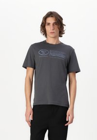 Camiseta de algodón gris con mangas cortas. Presenta texto impreso en azul y un logo en la parte frontal. Diseño de cuello redondo y ajuste relajado.