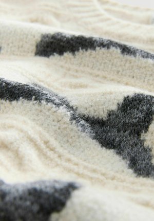 Raskaasti teksturoitu kerma- ja harmaasävyinen peitto, jossa on pehmeä ja ylellinen kangas vaihtelevilla sävyillä ja aaltoilevalla kuvioinnilla.
