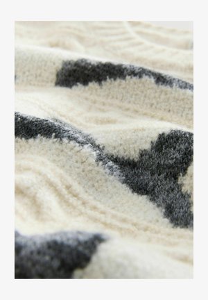 Teksturowany kremowo-szary pled z wzorem, wykonany z miękkiej, pluszowej tkaniny w różnych odcieniach i falistym wzorze.