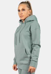 Felpa in cotone verde chiaro con cappuccio, dotata di lacci, tasca frontale a marsupio, polsini a coste e un sottile logo sulla manica.