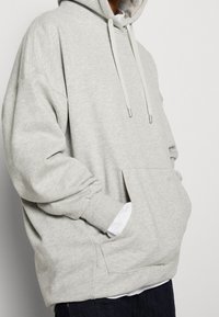Sudadera con capucha de color gris claro, con un bolsillo frontal tipo canguro, puños acanalados y cordones. Fabricada en una suave tela texturizada.