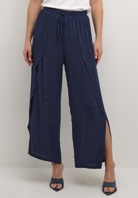 Marineblauwe wijde broek met een trekkoord in de taille en zijsplitten. Gemaakt van een lichtgewicht stof, met een gladde textuur en een vloeiend ontwerp.