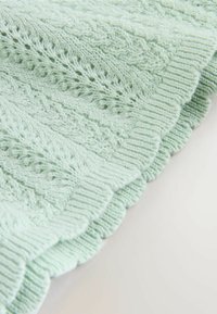 Adīta piparmētru zaļa sega ar teksturētu rakstu un ribotām malām, ar viļņotu apmali. Mīksta, viegla auduma.