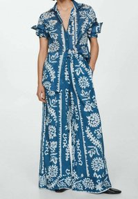 Ensemble deux pièces à imprimé bleu, composé d'un tissu léger ; comprend une chemise à manches courtes avec col et un pantalon à jambes larges ornés de motifs floraux blancs.