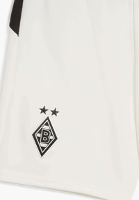 Biała tkanina z czarnym logo przedstawiającym kształt diamentu z literą "B" w środku oraz dwoma czarnymi gwiazdami powyżej.