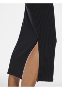 Nahaufnahme eines Beins einer Person, die gerippte schwarze Hosen mit einem seitlichen Schlitz trägt, durch den Haut sichtbar wird.