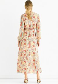 Floral maxi dress in pastel colors with long sleeves and a cinched waist. Features a scattered floral pattern and flowing skirt.