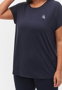 Granatowa koszulka z krótkim rękawem wykonana z miękkiego materiału, z małym trójkątnym wzorem na piersi. Luźny, swobodny krój z okrągłym dekoltem.