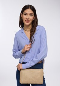 Camicia azzurra chiara con maniche lunghe, abbinata a una borsa a tracolla rettangolare in perline dorate con catena.
