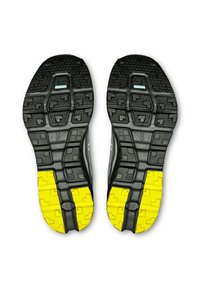 Schwarze Sportschuhsohlen mit strukturierten Griffmustern; verfügen über leuchtend gelbe Akzente und ein robustes Design für verbesserte Traktion.