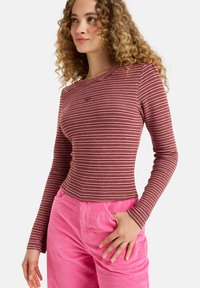 Gestreiftes Langarmoberteil in Weinrot und Rosa mit taillierter Passform. Rippstruktur und runder Halsausschnitt. Kombiniert mit rosa Cordhosen.