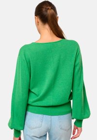 Pull en tricot vert avec une coupe décontractée, des manches larges et un ourlet côtelé. Le matériau semble doux et texturé, adapté pour une tenue décontractée.