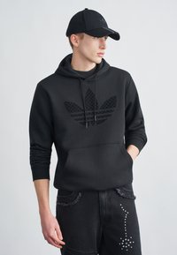 Felpa nera con logo nero texturizzato, coulisse e tasca a marsupio. Abbinata a jeans neri con dettagli consumati e borchiati.