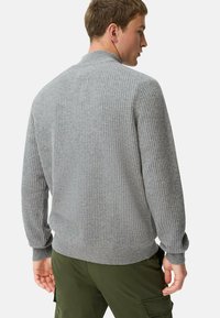 Grijze geribbelde trui met een hoge kraag, lange mouwen en een aansluitende tailleband, van achteren getoond op een model dat groene cargobroeken draagt.