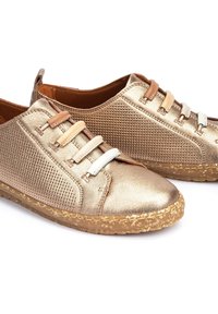 Chaussures décontractées en bronze métallisé avec côtés texturés, semelles en liège rembourrées, et bandes élastiques beige, tan et blanc remplaçant les lacets traditionnels.