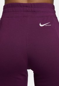 Leggings Nike violets avec une texture lisse et une taille haute. Présentent des détails de logo blanc près de la taille.