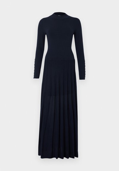 Długa granatowa dzianinowa sukienka z długimi rękawami, wysokim kołnierzem, dopasowaną talią, plisowaną spódnicą oraz guzikami na mankietach.