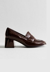 Mocasines de charol marrón con un tacón bloque rectangular. Cuenta con un vampir de costura y una tira decorativa en la parte delantera.