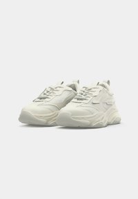 Zapatillas blancas gruesas con suelas gruesas, paneles de malla y cuero, cordones y lengüetas sobre un fondo blanco liso.