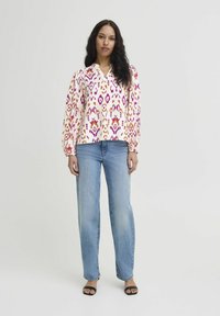 Top features a vibrant floral pattern in pink, orange, and yellow on a white background. Paired with light blue jeans and black sandals.