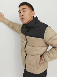 Giubbotto imbottito beige e nero con colletto alto, chiusura con zip e tasche laterali, caratterizzato da una texture trapuntata sul corpo.