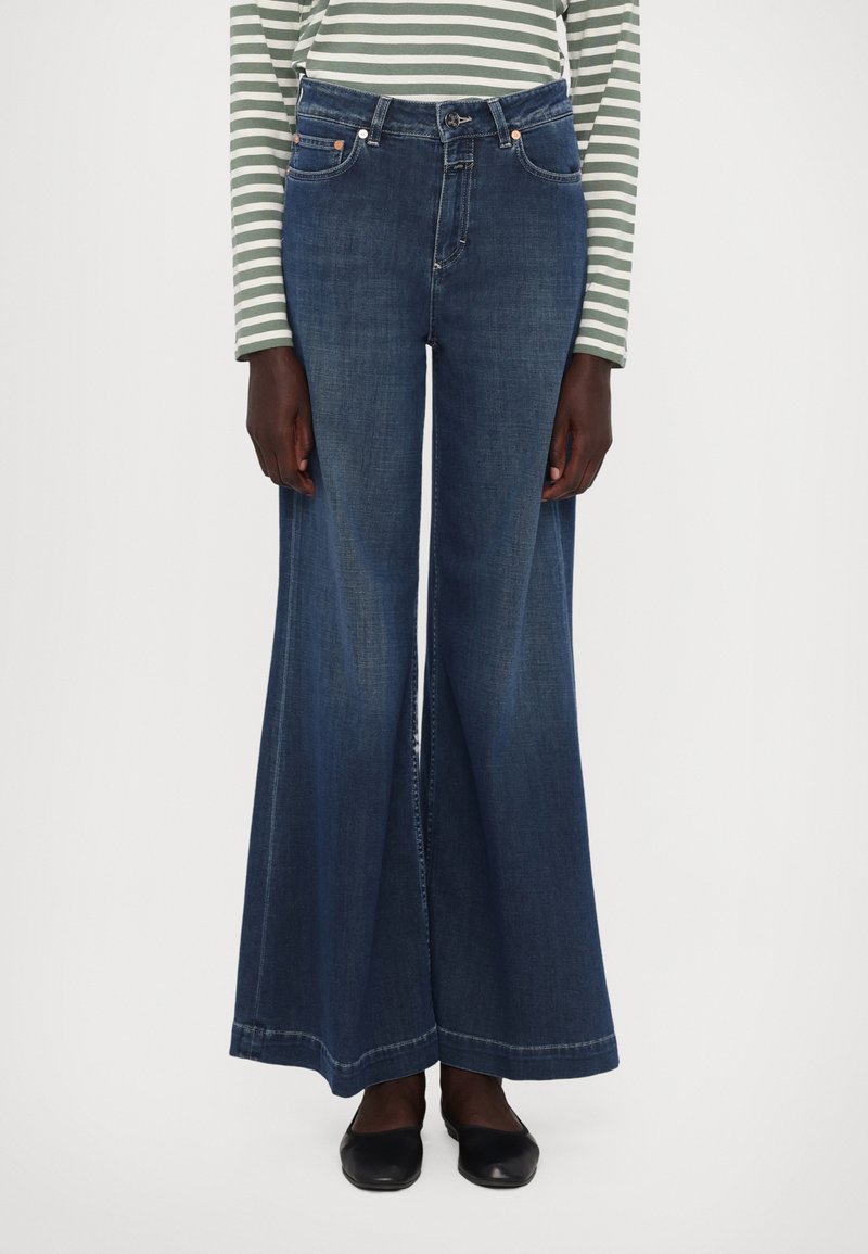 Bredde ben i denimjeans med en medium blå vask. Har fem lommer, glidelås foran og kontrasterende sømmer. Bredder seg ut fra kneet og ned.