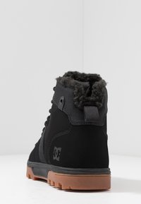 Czarny wysokiego kroju but z miękkim, wełnistym kołnierzem, gumową podeszwą oraz sznurowaniem z przodu; posiada małe logo po boku.