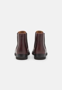 Bottes basses en cuir bordeaux avec panneaux latéraux élastiques, bouts arrondis et semelles en caoutchouc noir. L'intérieur est doté d'une doublure lisse beige.