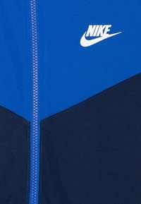 Nike ar rāvējslēdzēju, kas sastāv no zilas augšdaļas un tumši zilas apakšdaļas. Tam ir balta logo uz krūtīm un strukturēta auduma.