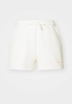 Hvite bomullsshorts med elastisk midje og en knyttet detalj. Har lommer på sidene og en liten trykt logo i lys orange.